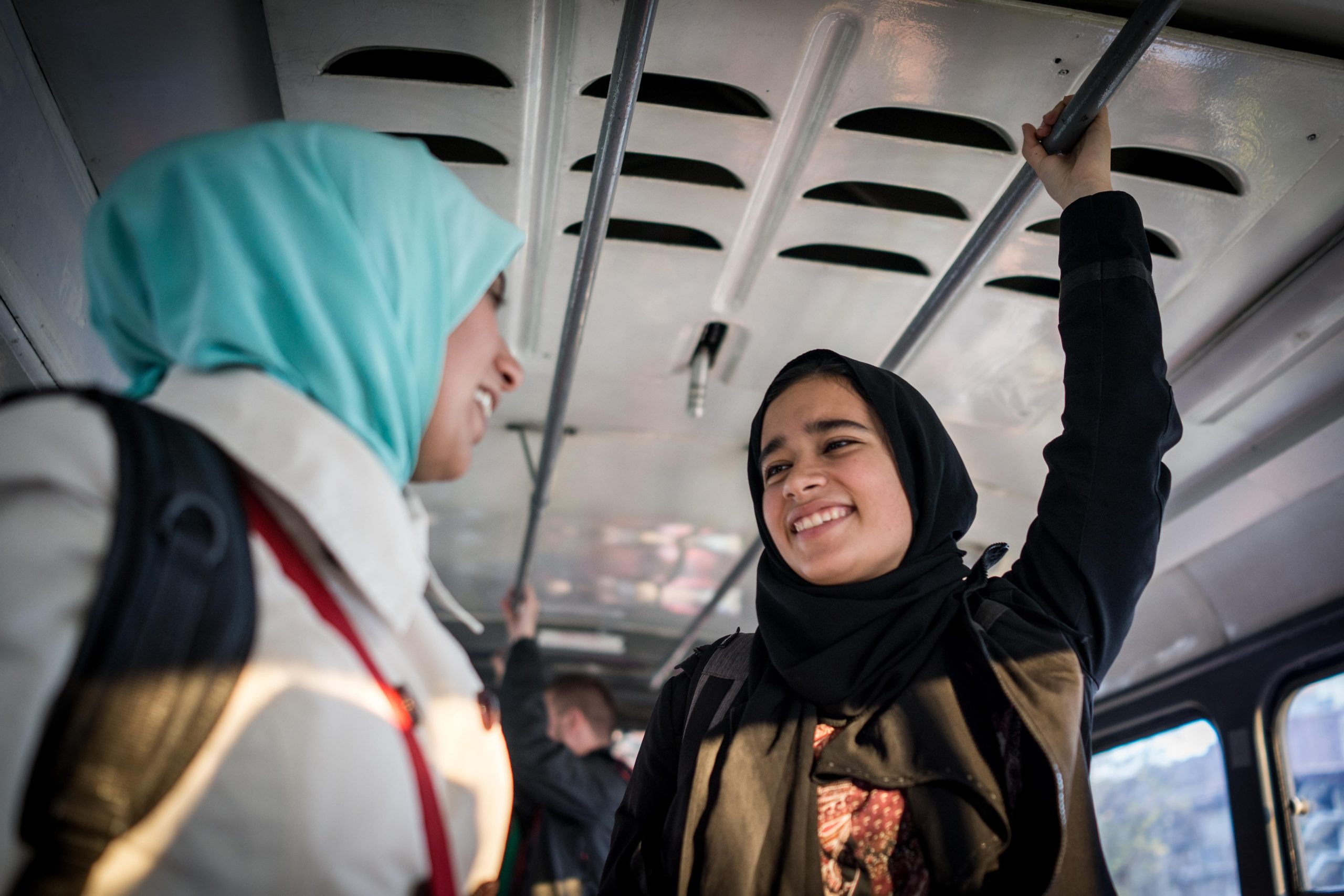 Two young women wearing hijab talking while riding on the bus