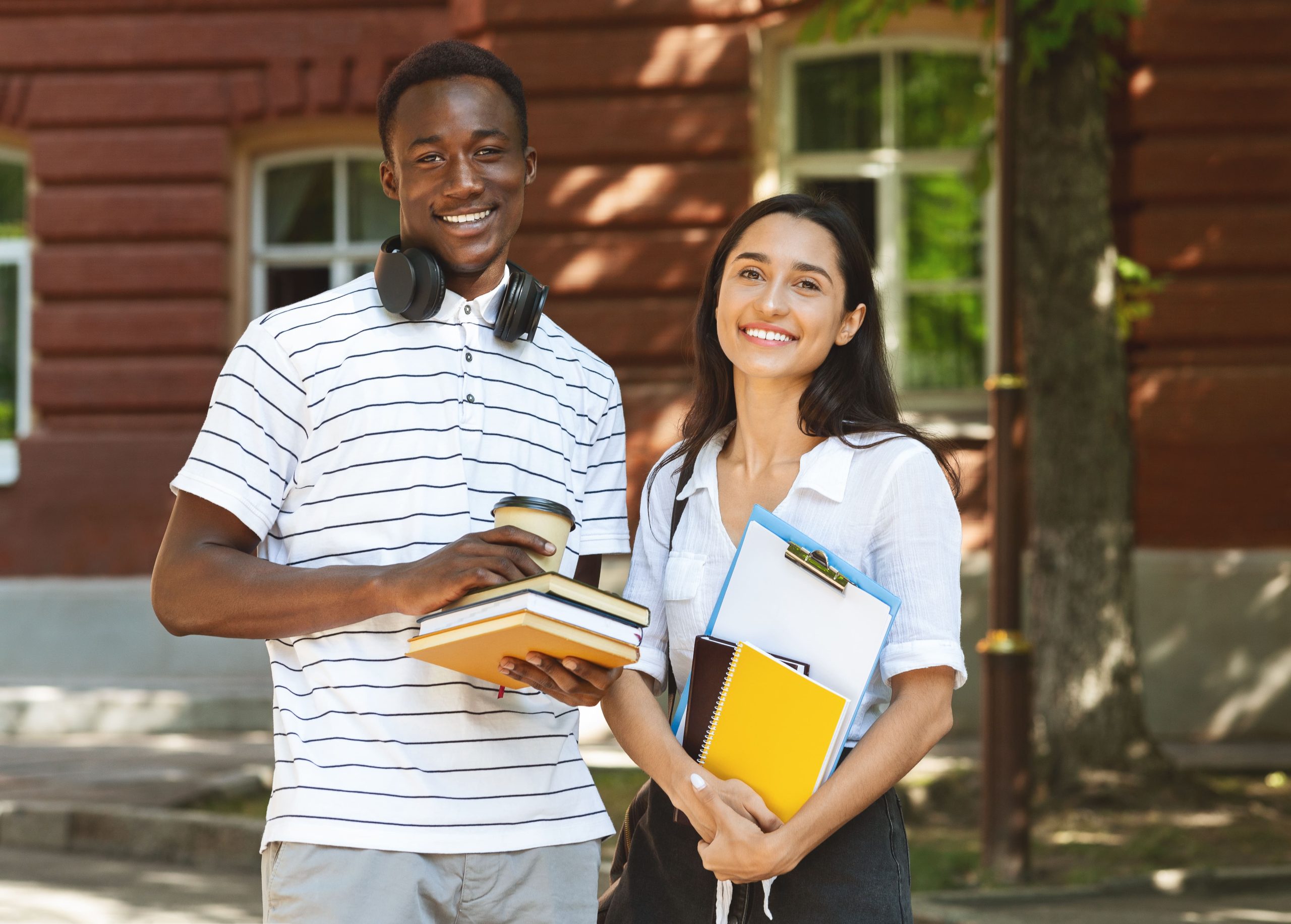 Young man and young woman smiling for the camera while holding books