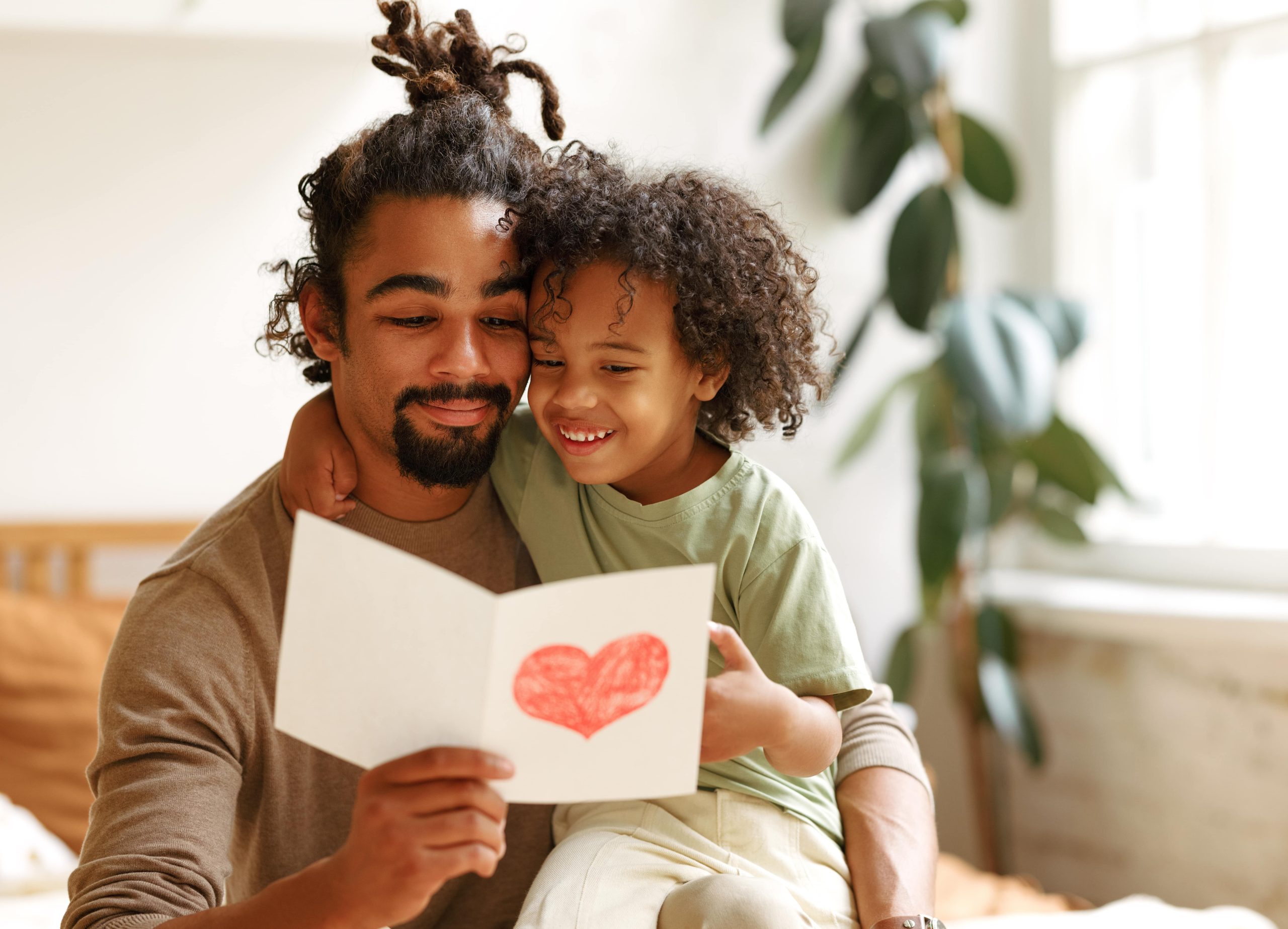 Kid sitting on father's lap while father holds a card with a heart on it