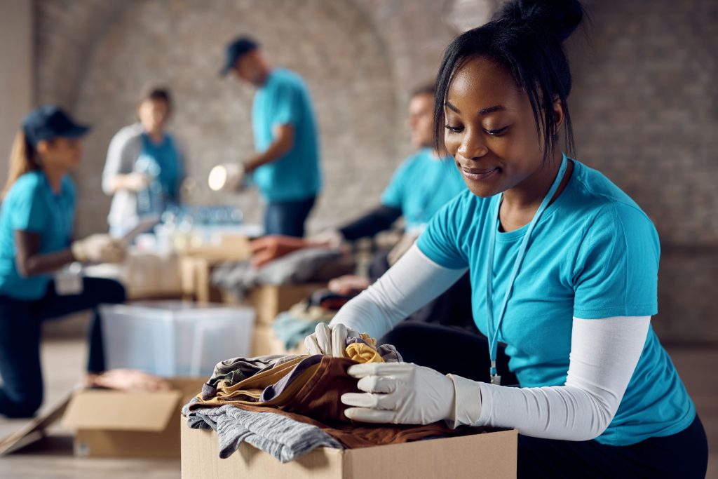 Woman packing clothing donations while other volunteers pack other donations in the back