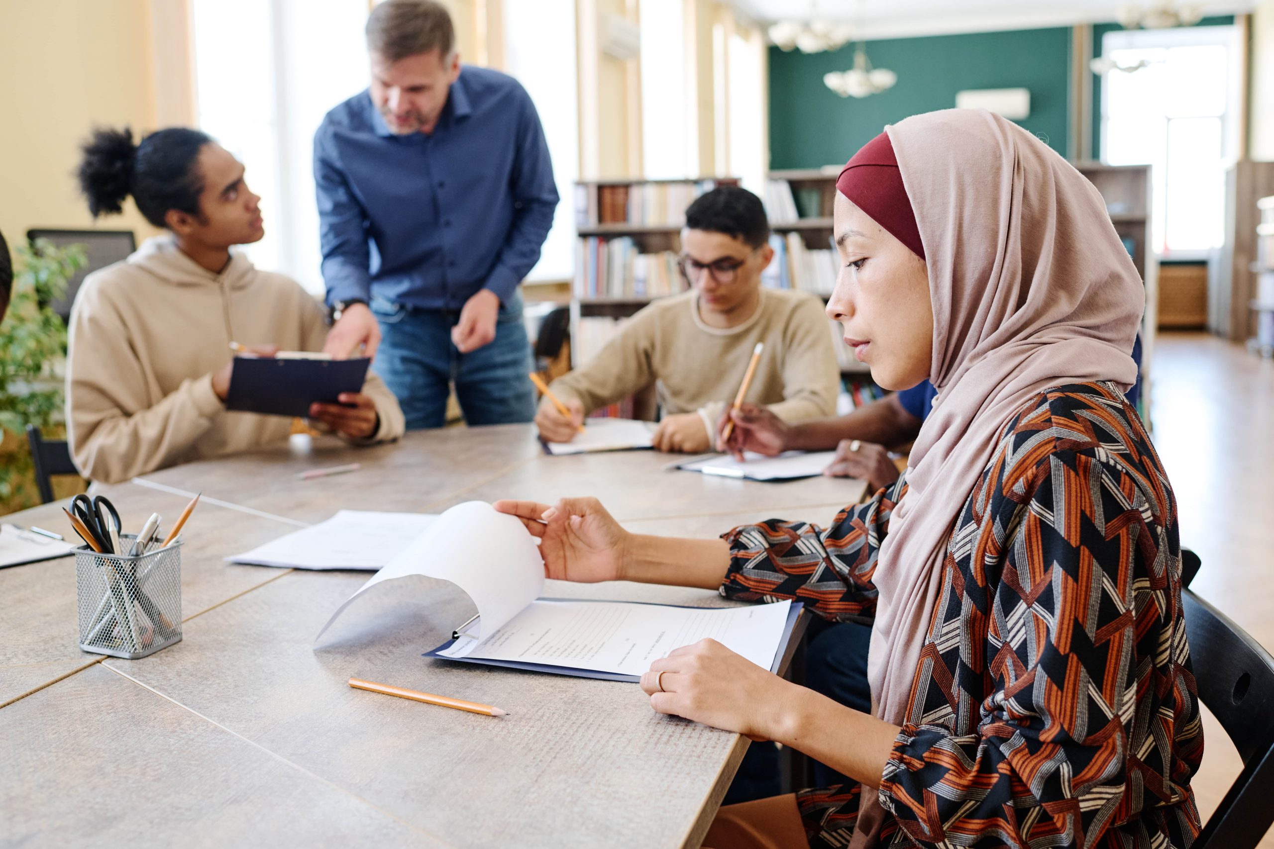 A group of multicultural people talking to each other while studying in a table, with focus on woman with Hijab
