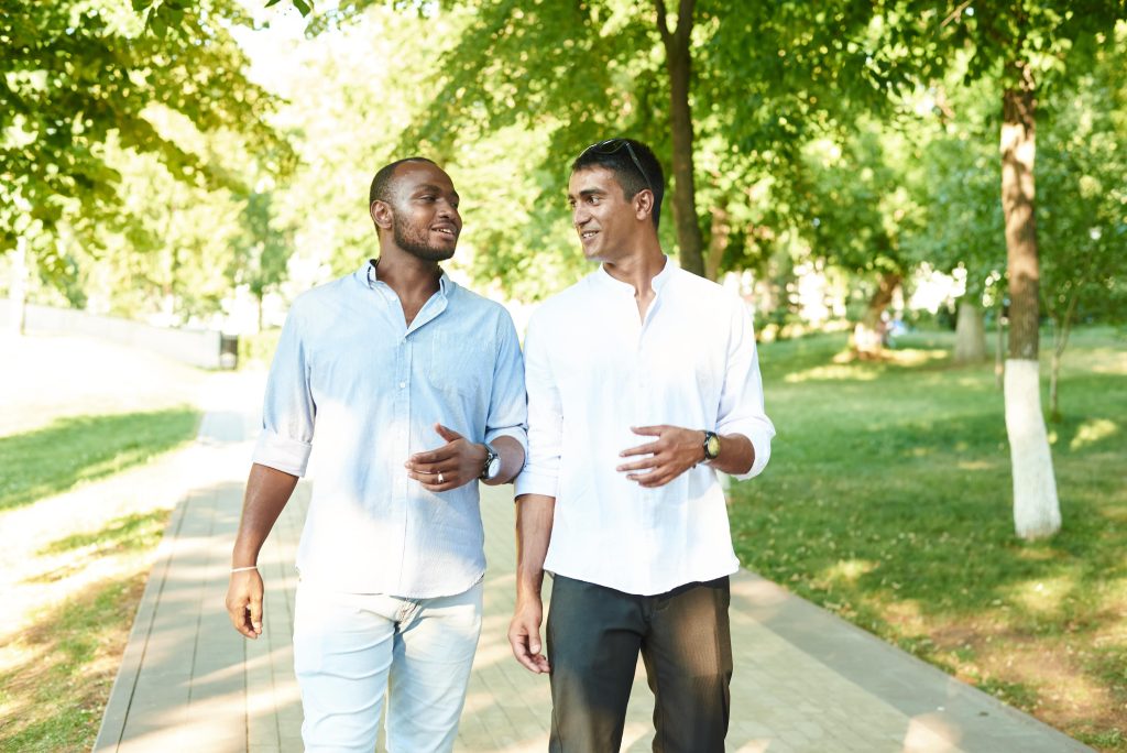 Two multicultural men talking to each other while walking in the park