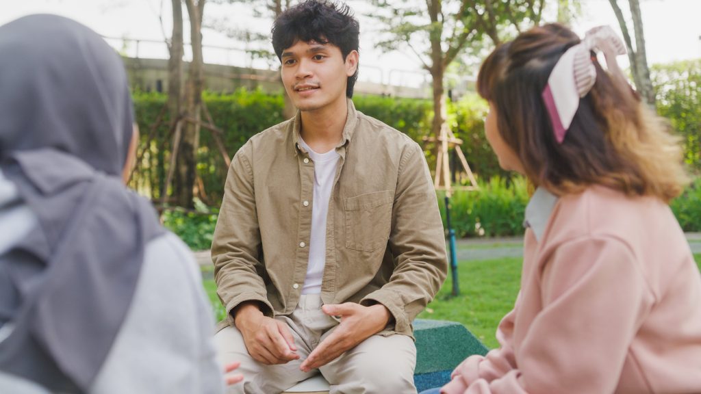 Young man talks to two multicultural young woman at the park